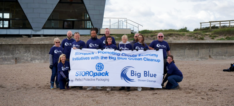 Plusieurs personnes posent pour une photo de groupe sur la plage en tenant une bannière de l’organisation Big Blue Ocean Cleanup