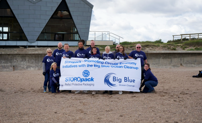 Plusieurs personnes posent pour une photo de groupe sur la plage en tenant une bannière de l’organisation Big Blue Ocean Cleanup