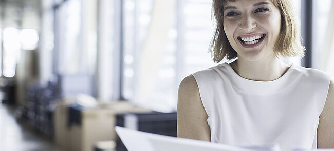Eine junge Frau steht mit Dokumenten in einem Büro und freut sich