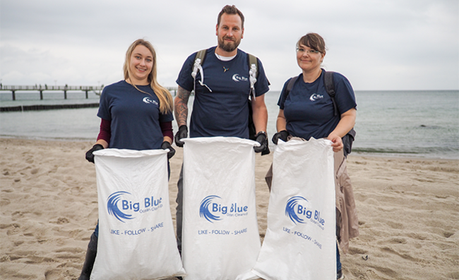 Trois employés Storopack debout sur la plage, tenant des sacs poubelles