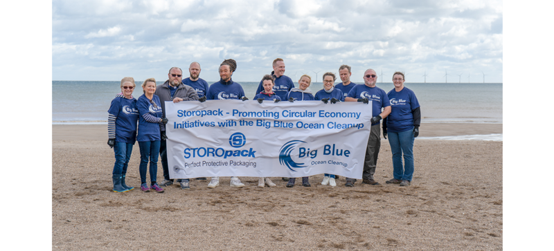 Plusieurs personnes posent pour une photo de groupe sur la plage en tenant une bannière de l’organisation Big Blue Ocean Cleanup