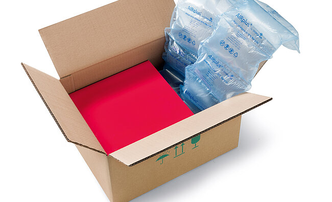 Un carton contenant une boîte rouge et des coussins d’air 100% RECYCLED 